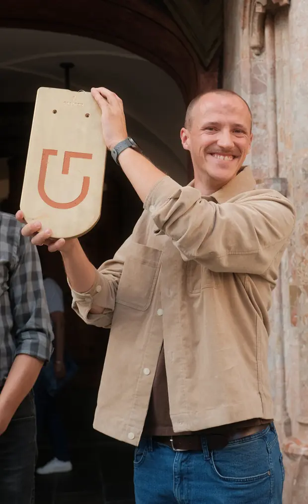 A man holding up a wooden shingle printed with the award’s symbol