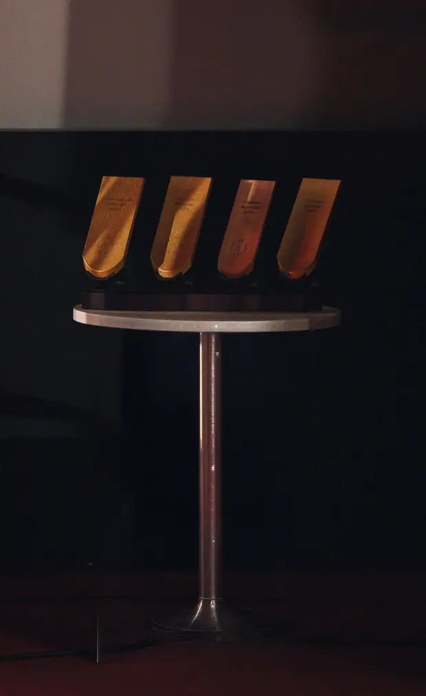 Four golden shingle trophies on a high table on stage