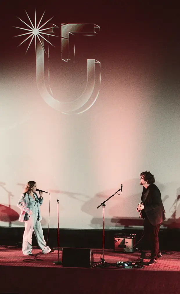 Two musicians on stage beneath the shingle on the cinema screen